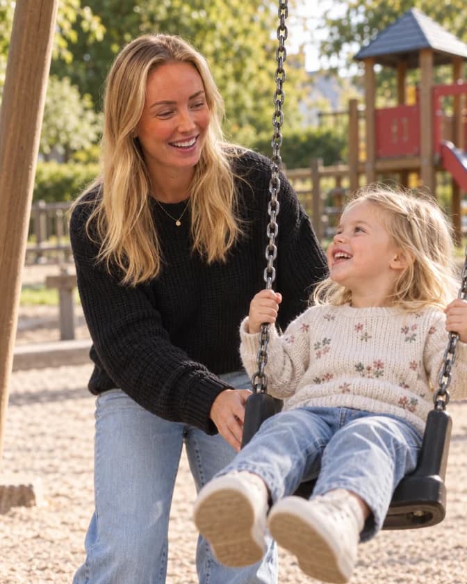 En nanny gungar en skrattande flicka på en lekplats